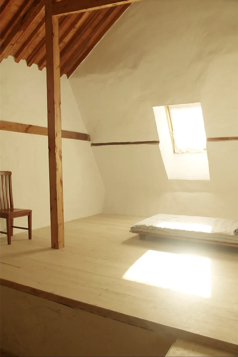 Une chambre Mansarde : plafond en pente, poutres apparentes.